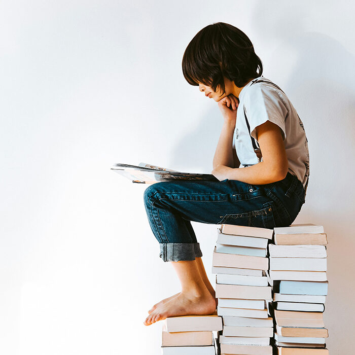 Ett barn sitter på en hög stapel av böcker och läser.